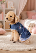 Mavi etekli koyu kar yıkama denim köpek elbisesi giyen toy poodle ev ortamında yandan görünümde oturuyor